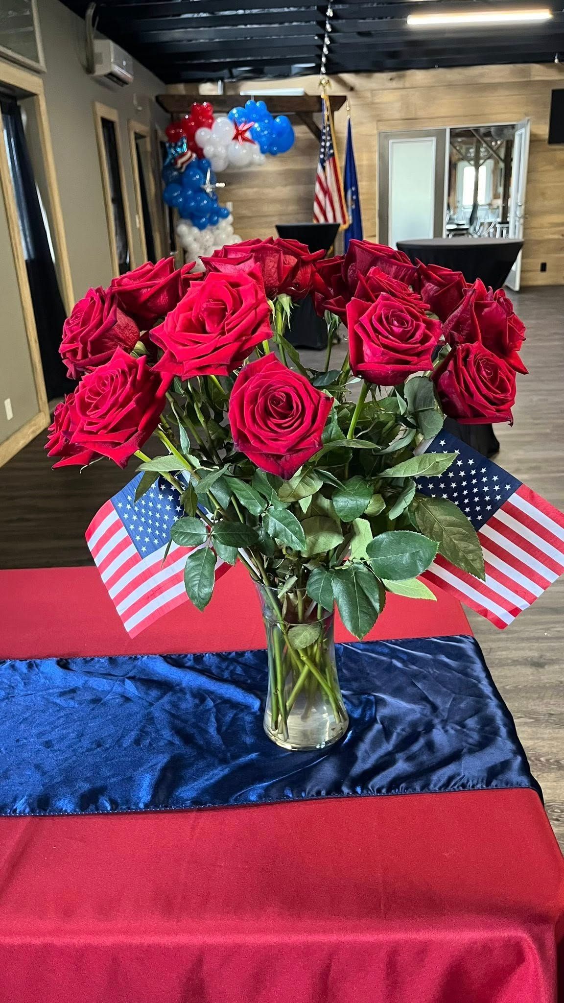 A vase filled with red roses and american flags on a table.