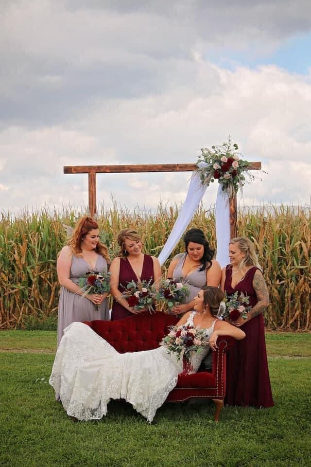 A bride and her bridesmaids are posing for a picture in front of a corn field.