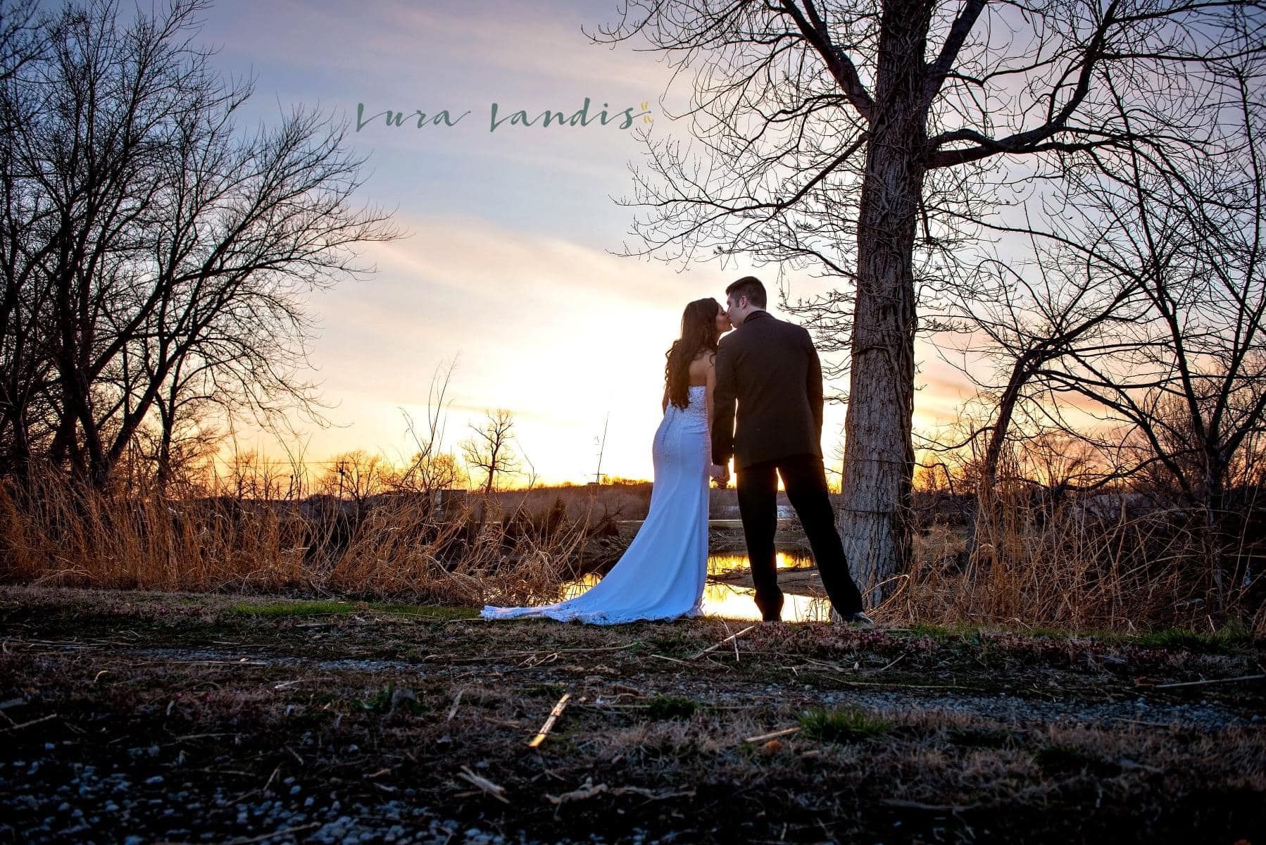 A bride and groom are standing under a tree at sunset