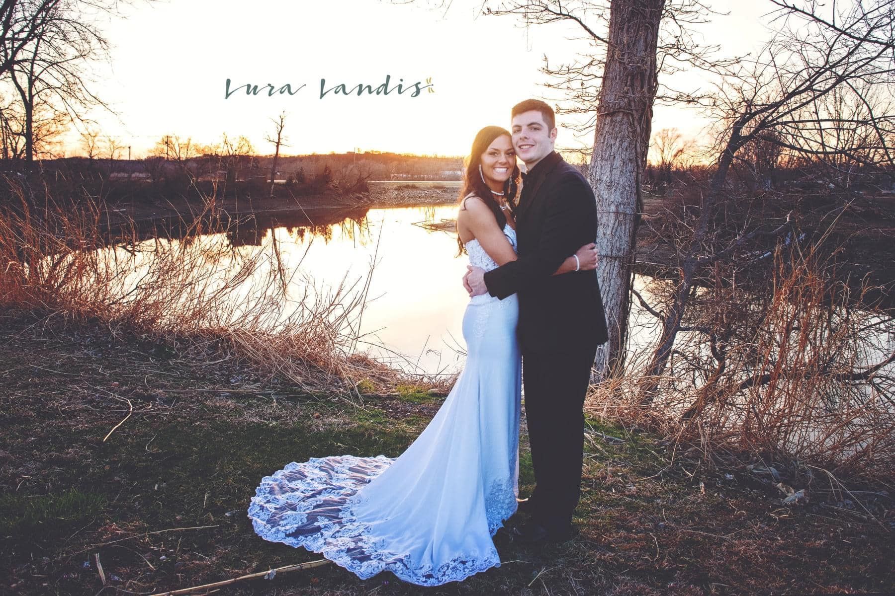 A bride and groom pose for a picture in front of a lake