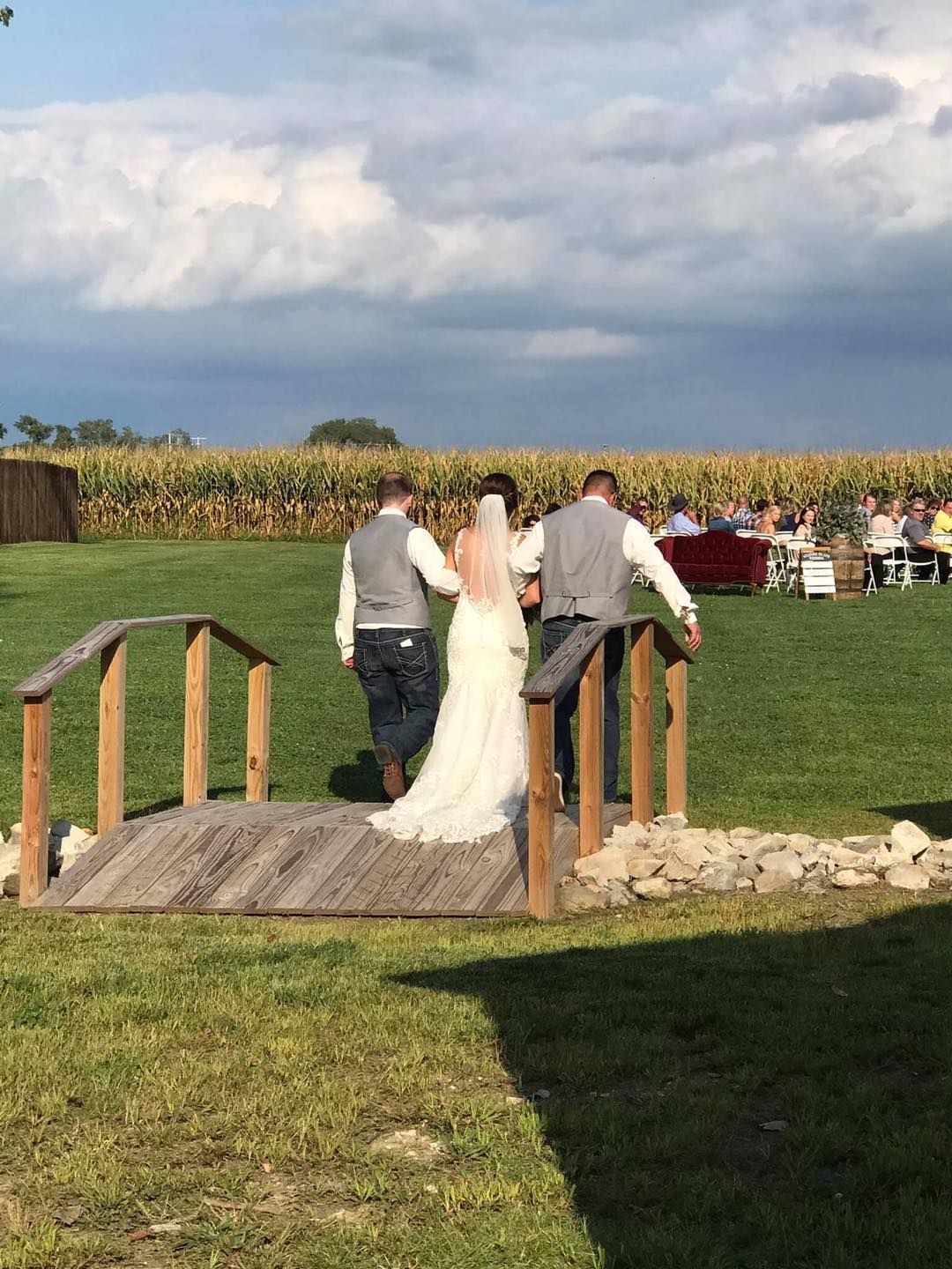 A bride and groom are walking across a wooden bridge.