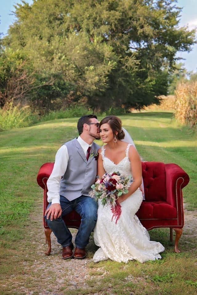 A bride and groom are kissing while sitting on a red couch.