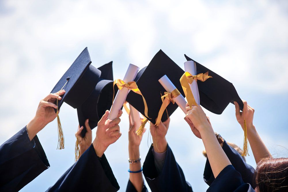 A group of graduates are holding their caps and diplomas in the air.
