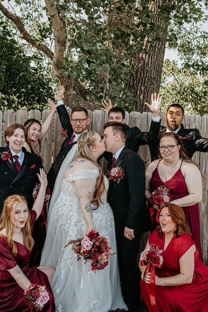 A bride and groom are kissing in front of their wedding party.