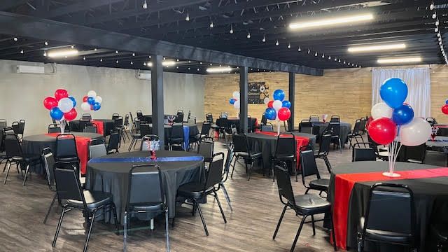 A large room filled with tables and chairs decorated with red , white and blue balloons.