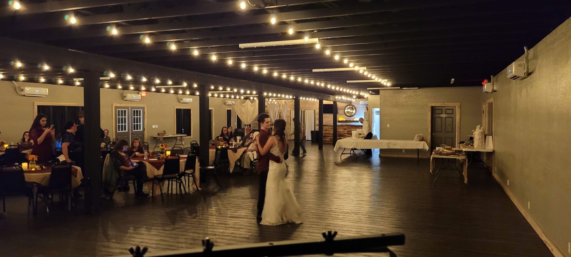 A bride and groom are dancing in a large room at a wedding reception.