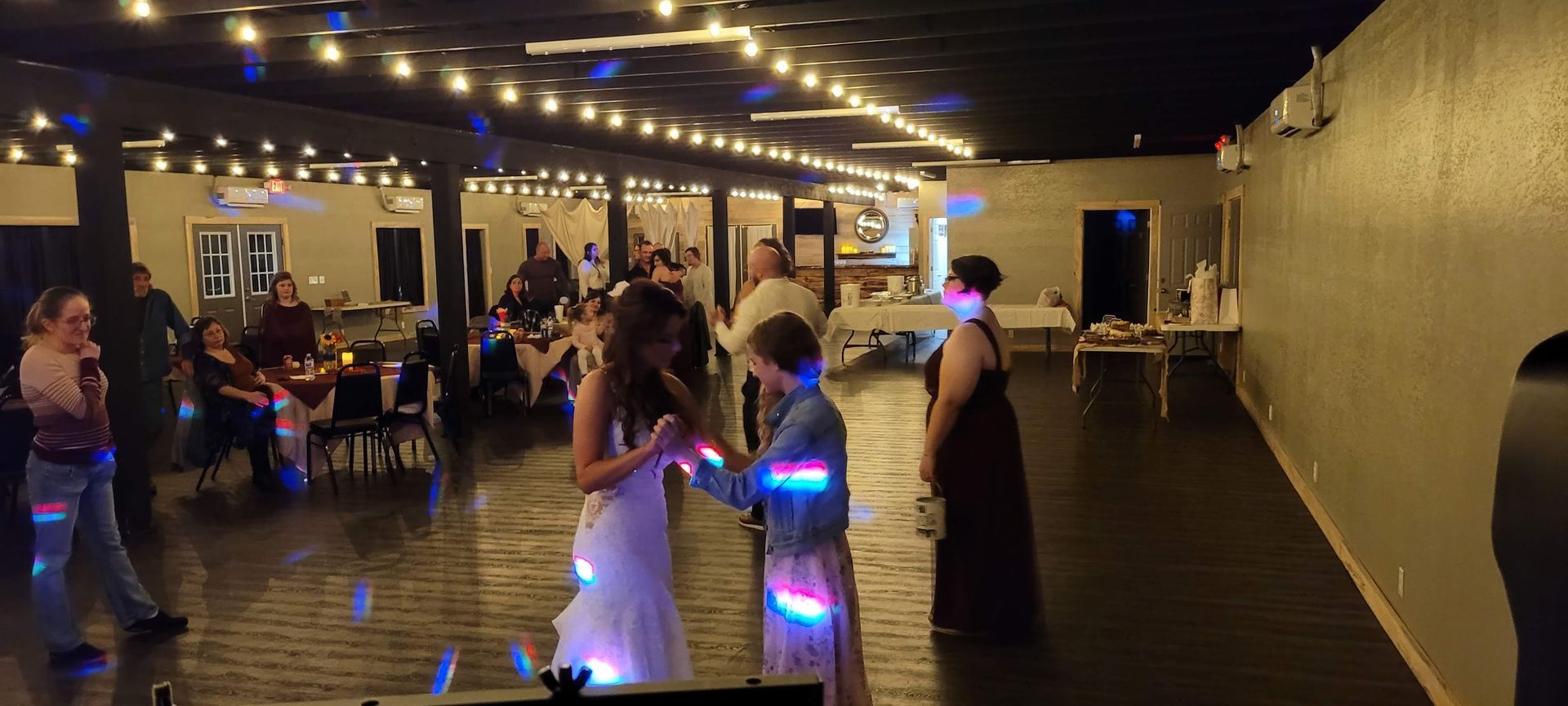 A group of people are dancing in a large room at a wedding reception.
