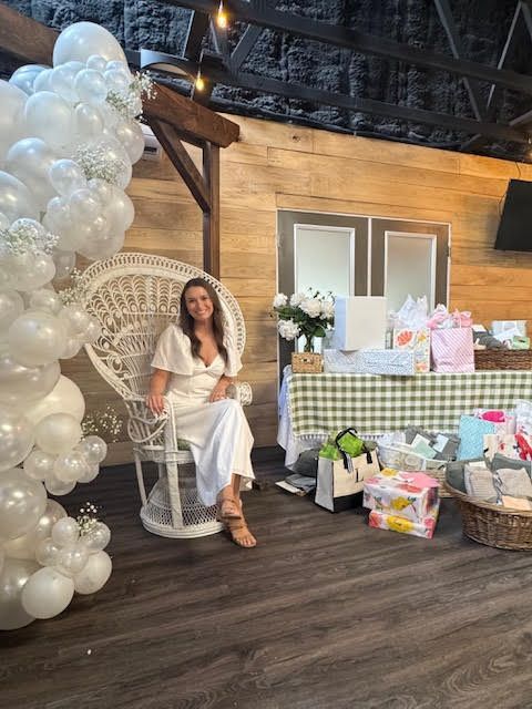 A woman is sitting in a chair in front of a wall of white balloons.