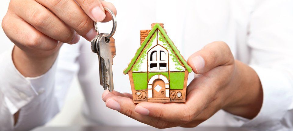 A man's hands holding a model of a house in terracotta, green and white, and a bunch of keys