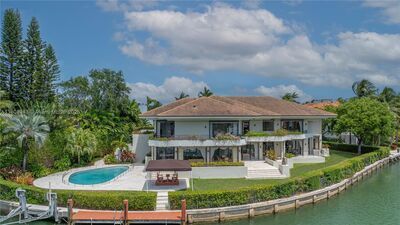 Luxurious waterfront home with pool and dock, surrounded by lush greenery under a blue sky.