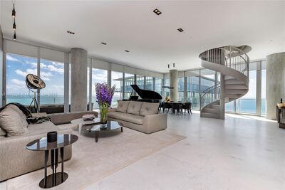Luxury apartment living room with a spiral staircase, ocean views, and a grand piano.