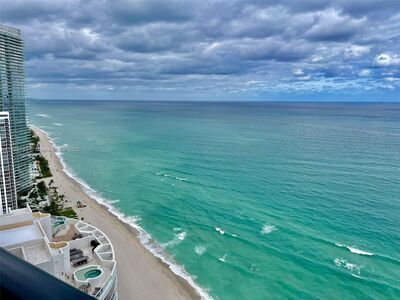 View of ocean and beach from a high-rise building on a cloudy day, turquoise water, white sand.