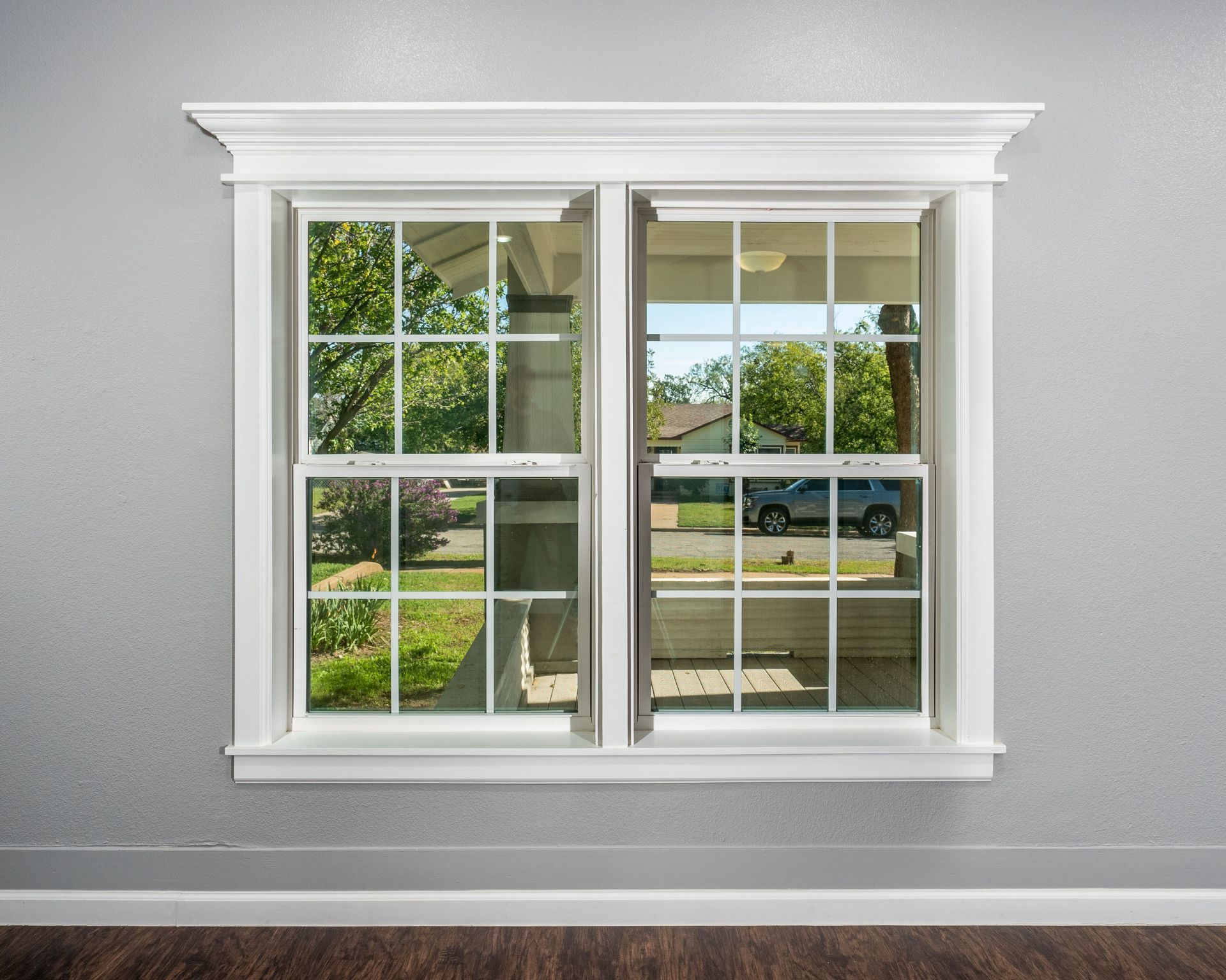 An empty room with two windows and a reflection of a car in the window.