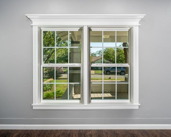 An empty room with two windows and a reflection of a car in the window.
