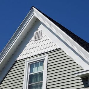 Close-up of a house's roofline with white trim, gray shingles, a window, and a blue sky.