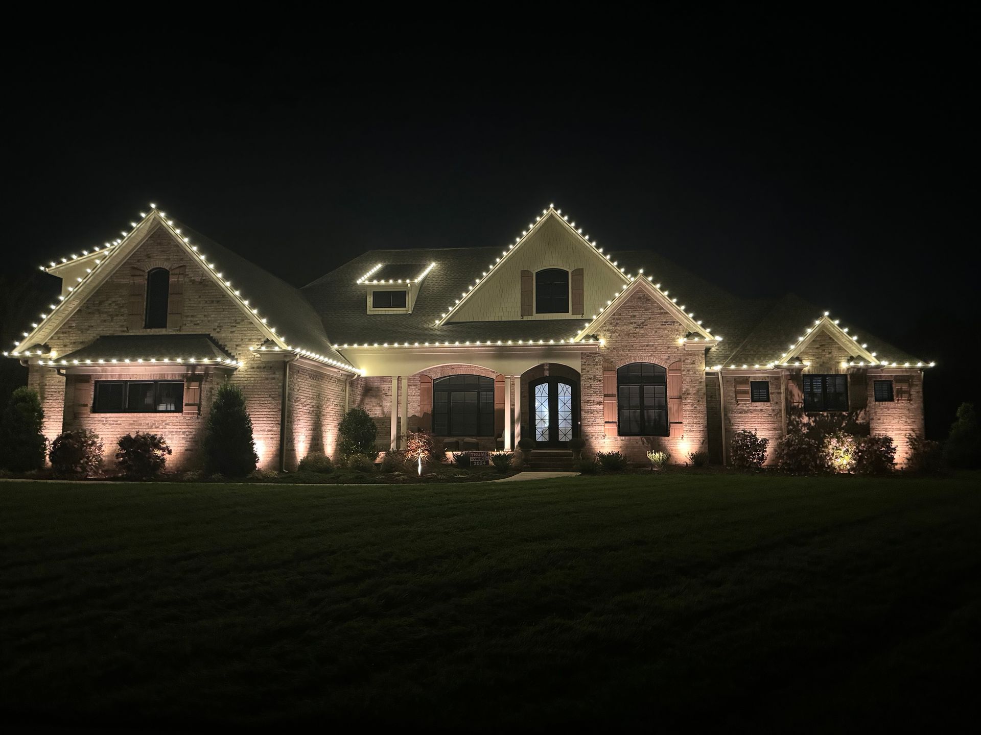 Elegant two-story brick house with warm white roofline Christmas lights at nigth