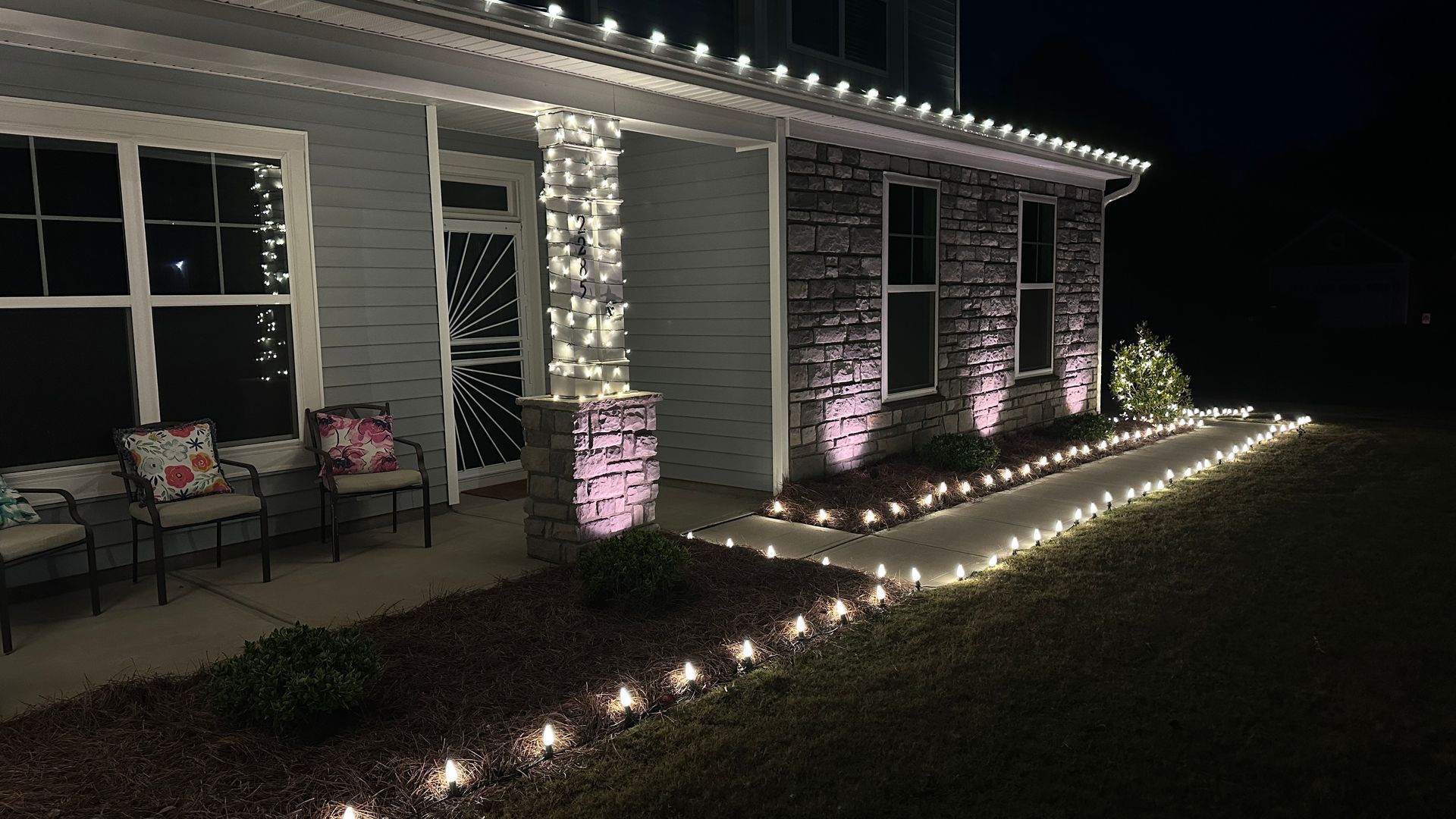 House decorated with white lights for the holidays. Porch, trim, and walkway are illuminated at night.