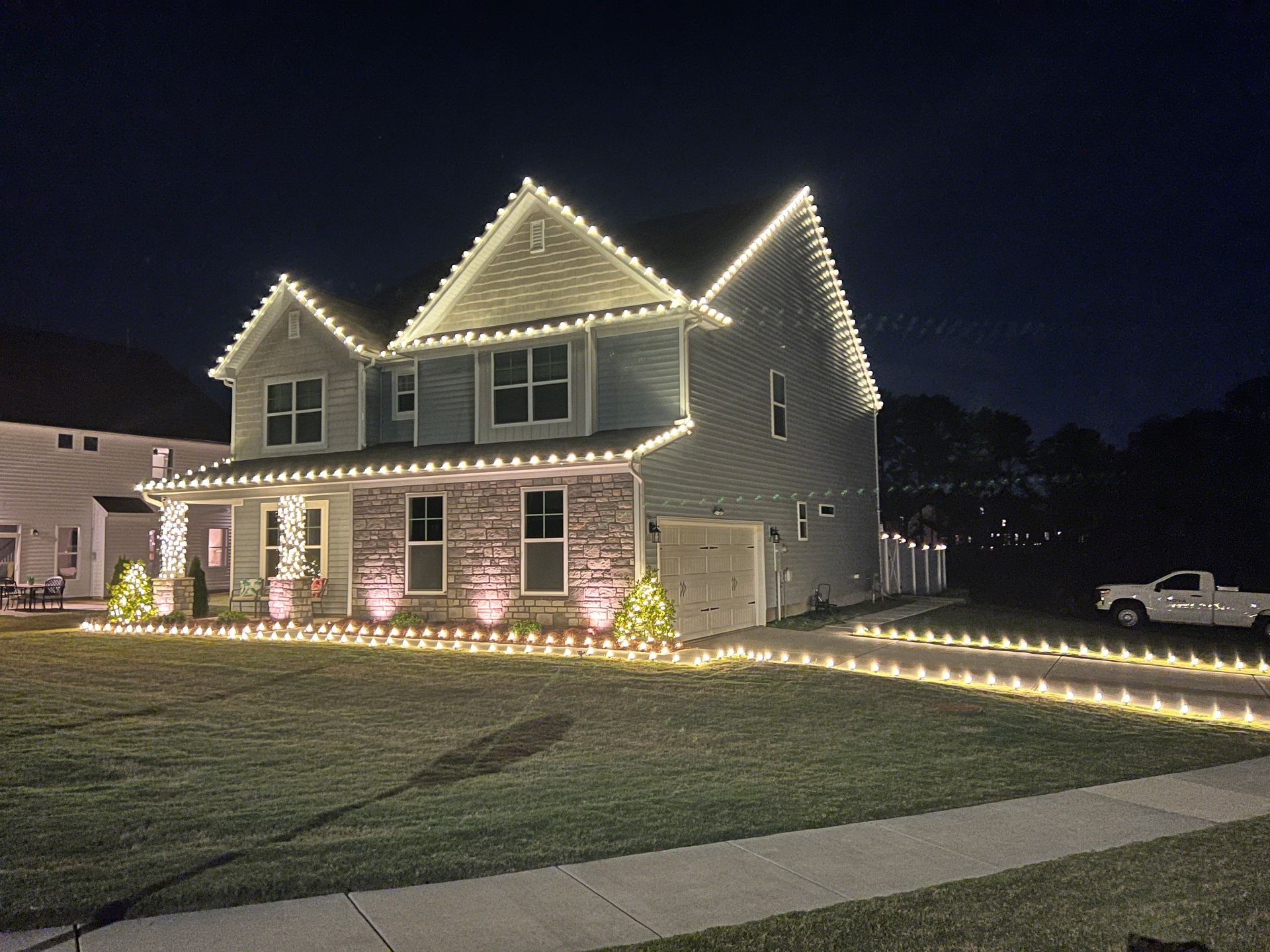 House decorated with white Christmas lights along the roofline, windows, and driveway; at night.