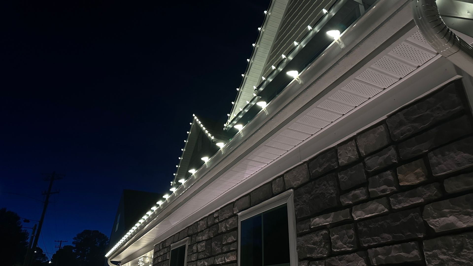 House exterior at night with white lights outlining roof and windows against dark sky.