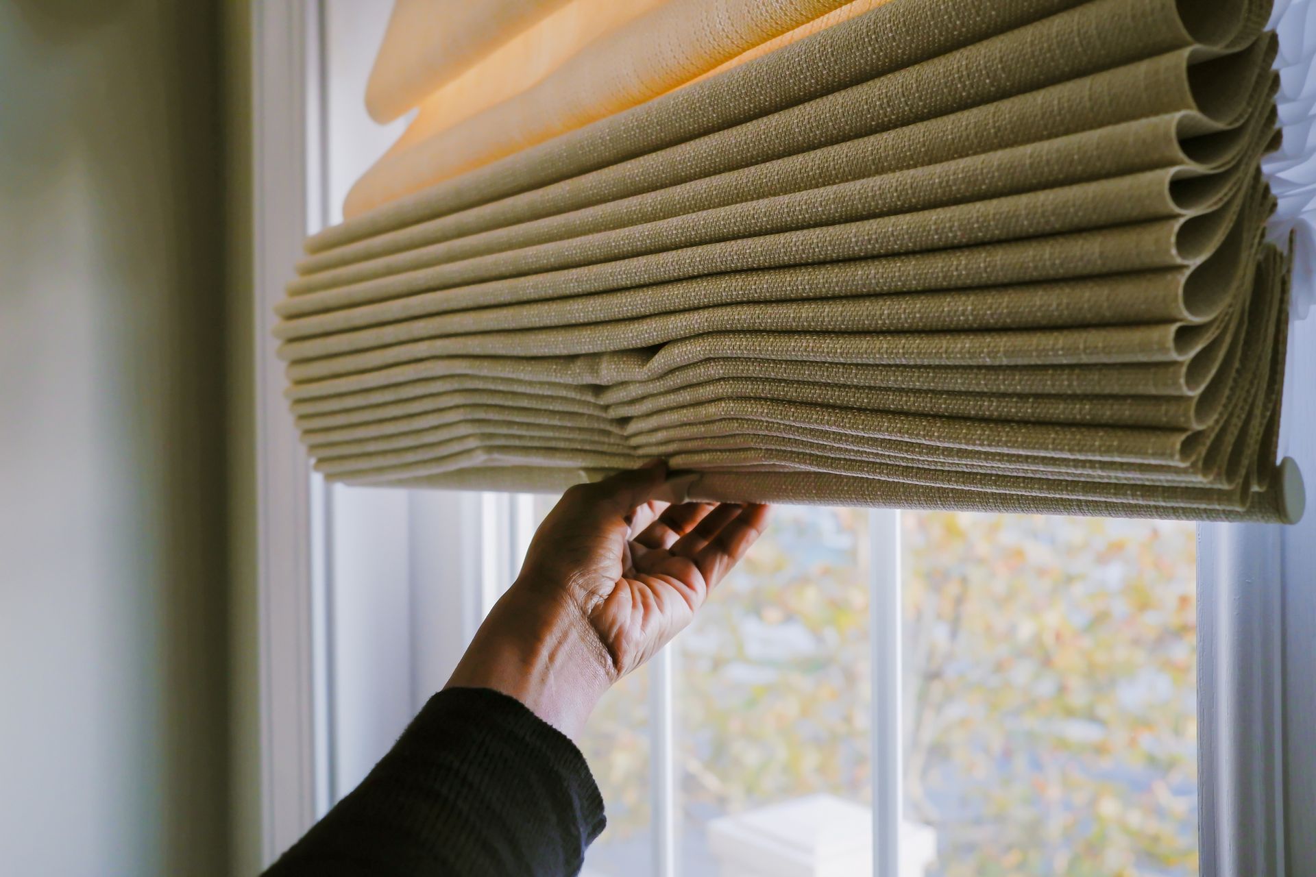 An individual pulling down window shades, creating a cozy atmosphere in a sunlit space.