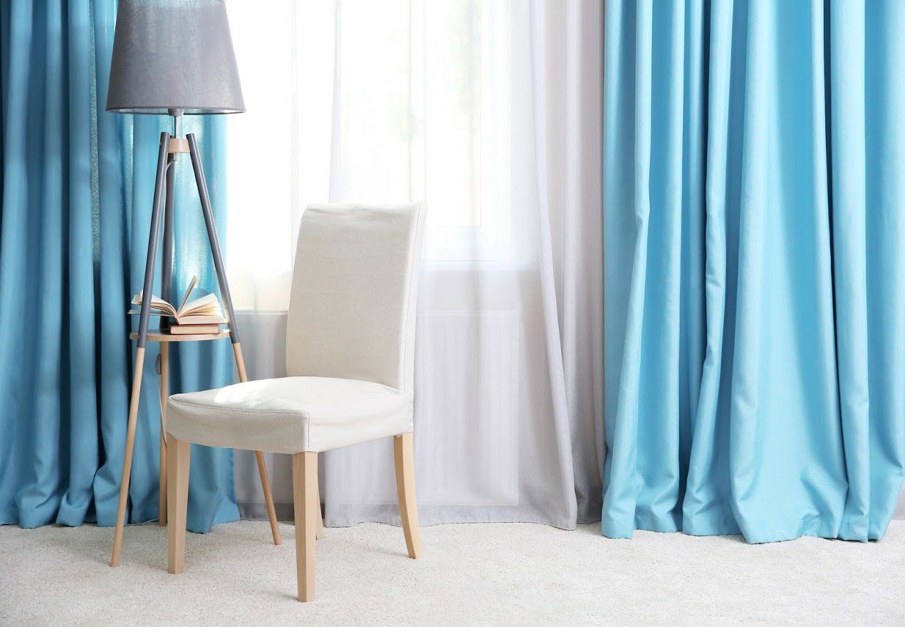 There is a chair and a lamp in the room with blue curtains.