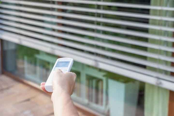 A person is holding a remote control in front of a window.