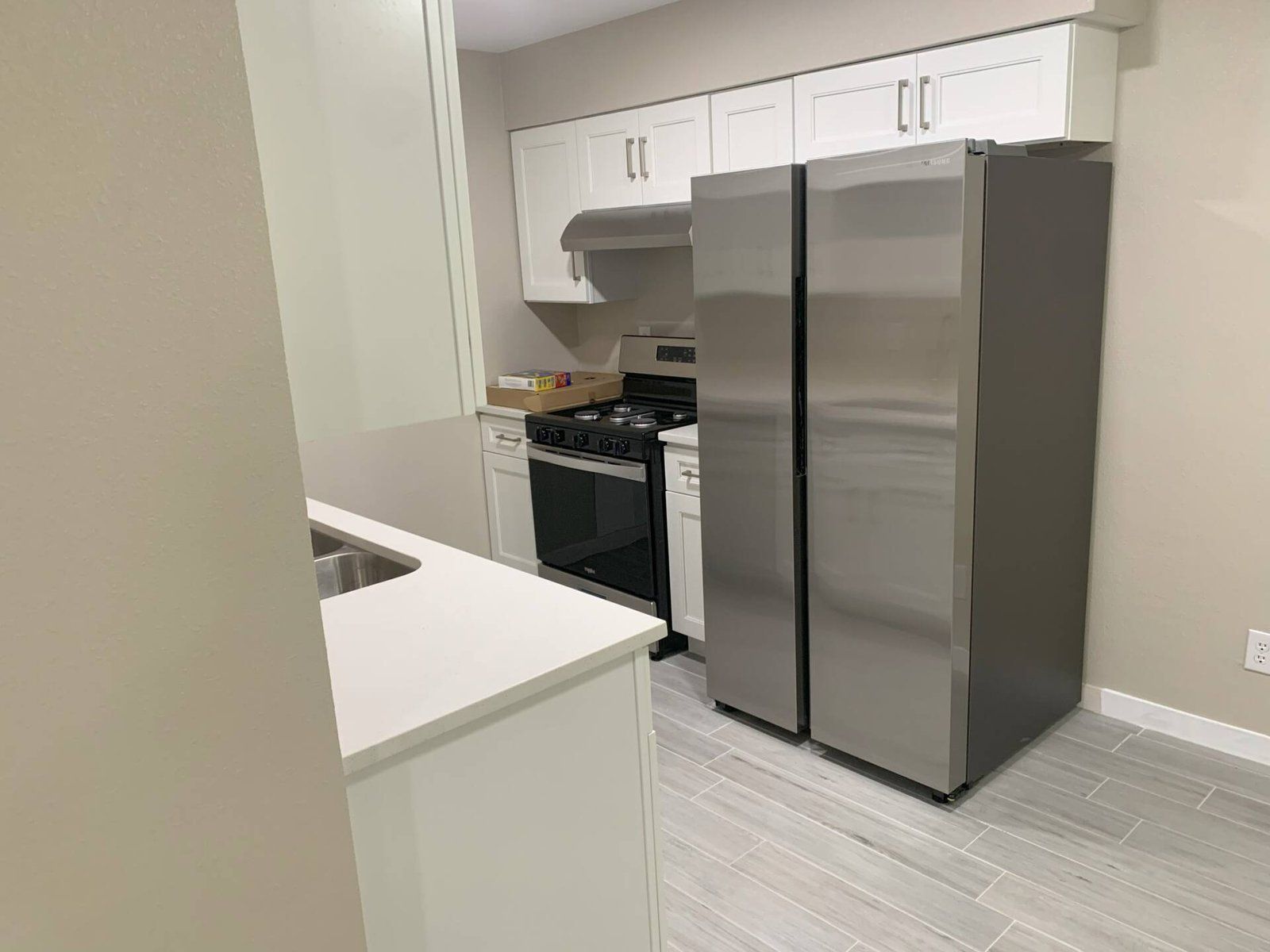 Kitchen with white cabinets, stainless steel refrigerator, and gray tile flooring.