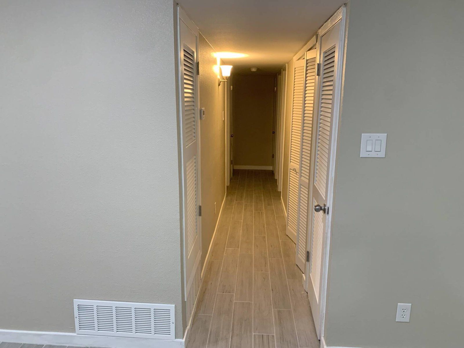 Narrow hallway with tan walls, tiled floor, and two louvered doors.
