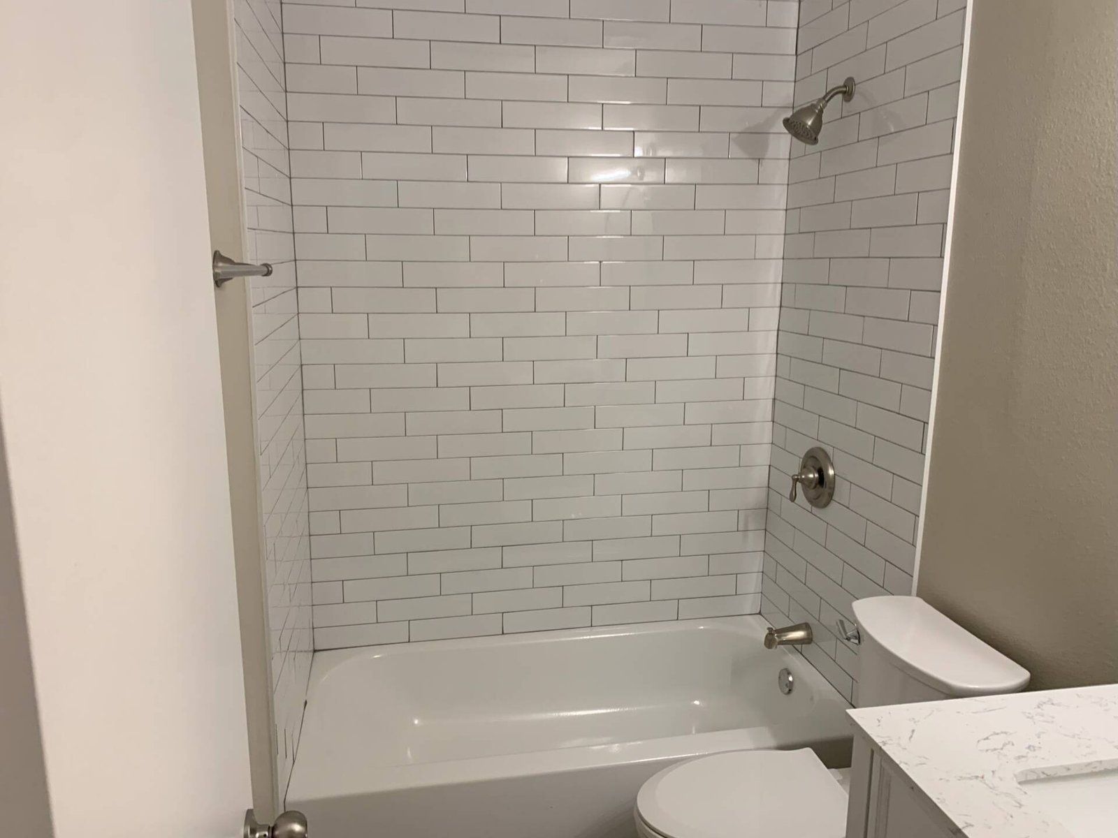 White tiled shower with silver fixtures and toilet.