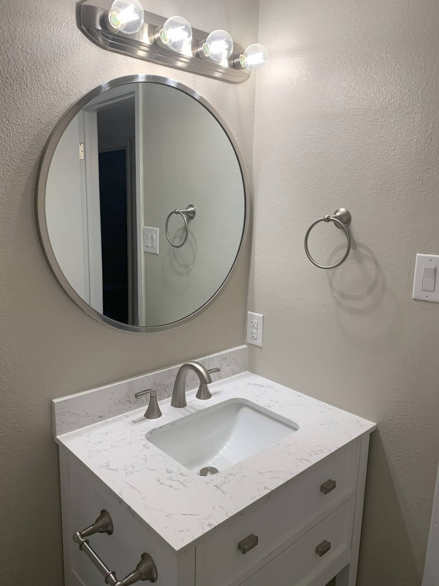 Bathroom with a round mirror, white vanity, and brushed nickel fixtures.