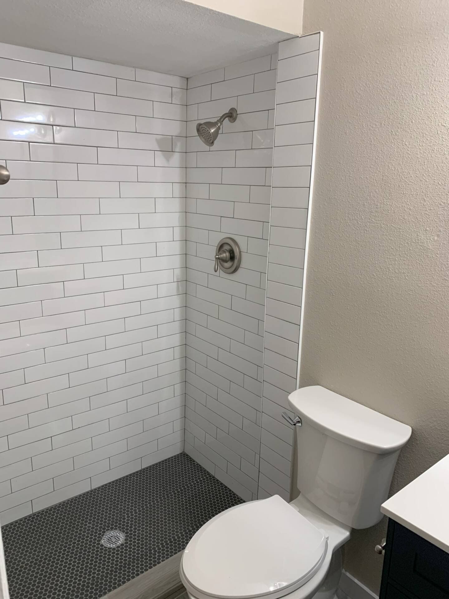 Bathroom with white brick-style tiled shower, black floor, toilet, and tan wall.