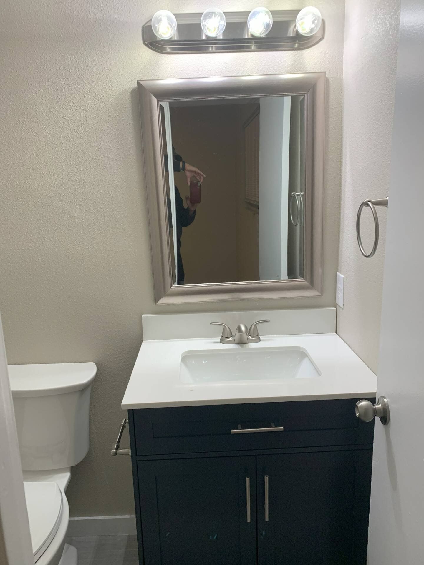 Bathroom with black vanity, white countertop, and square mirror, next to a toilet and door.