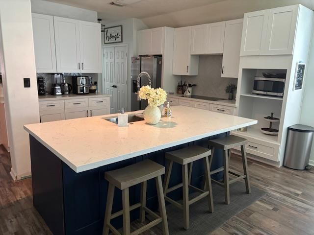 Modern kitchen with white cabinets, blue island, white countertop, and stools.