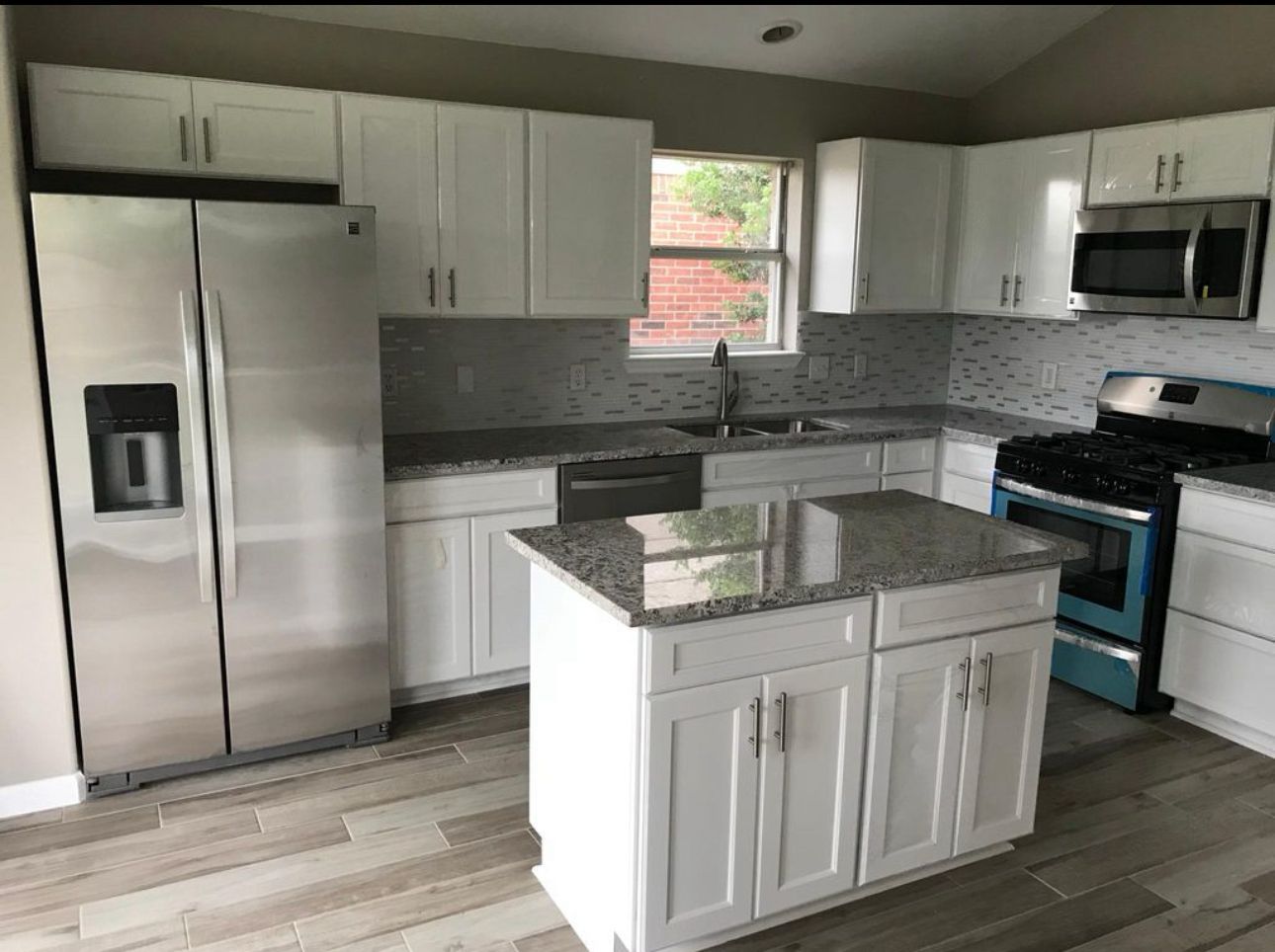White kitchen with stainless steel appliances, granite countertops and island, and light wood flooring.