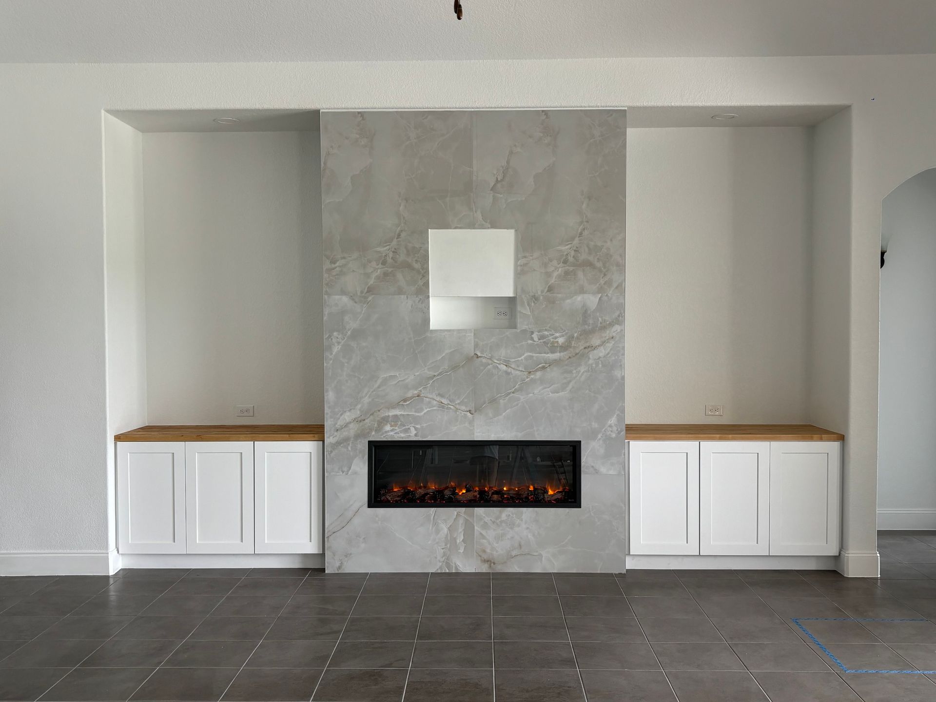Fireplace with grey stone, white cabinets, and an electric fire.