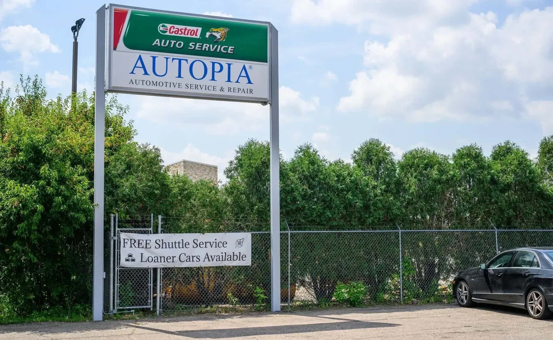 Sign for Autopia auto service with a Castrol logo, in front of a green hedge and parked car | Autopia Auto Repair - Bloomington