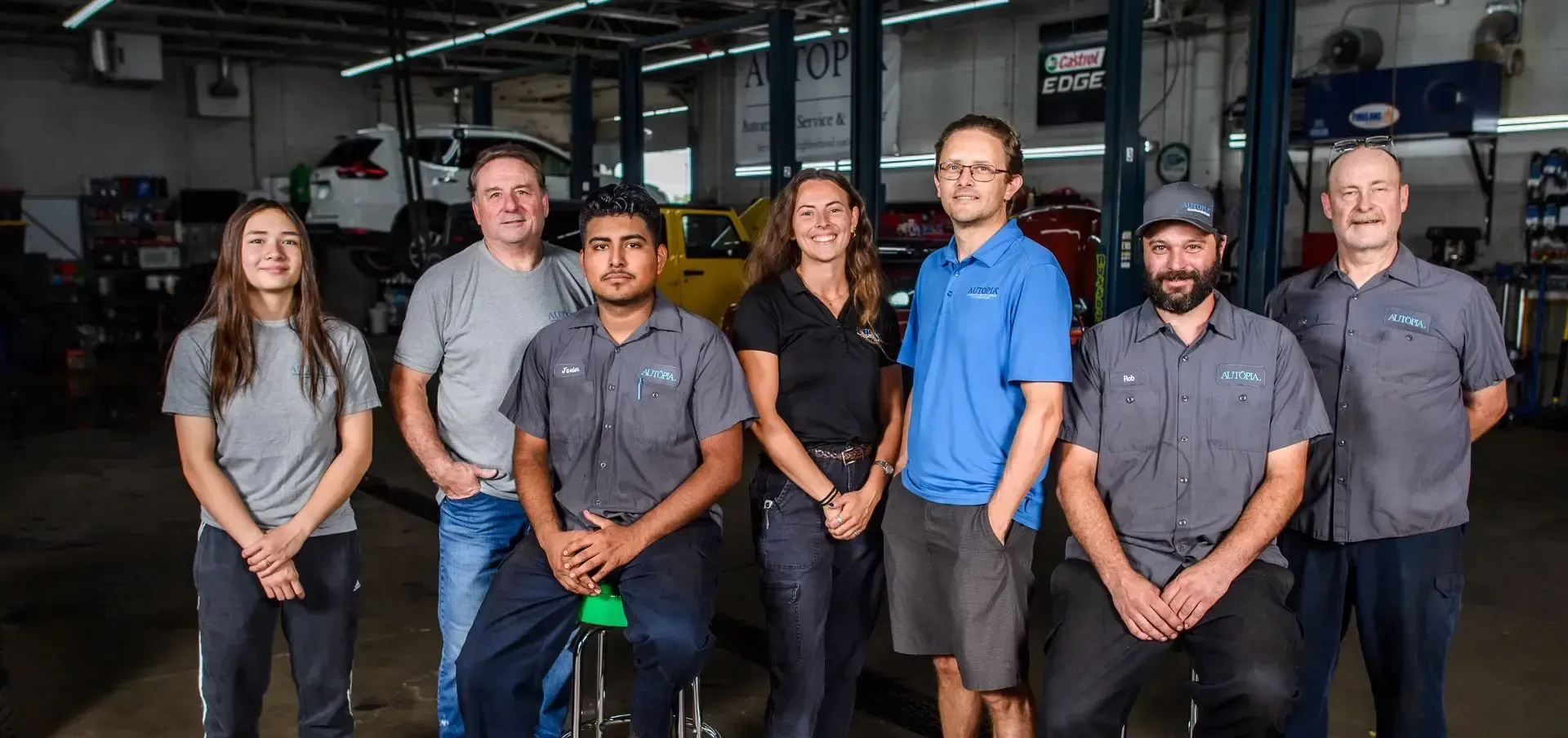 Group of seven people posing in an auto repair shop. They are smiling, wearing work uniforms | Autopia Auto Repair - Bloomington