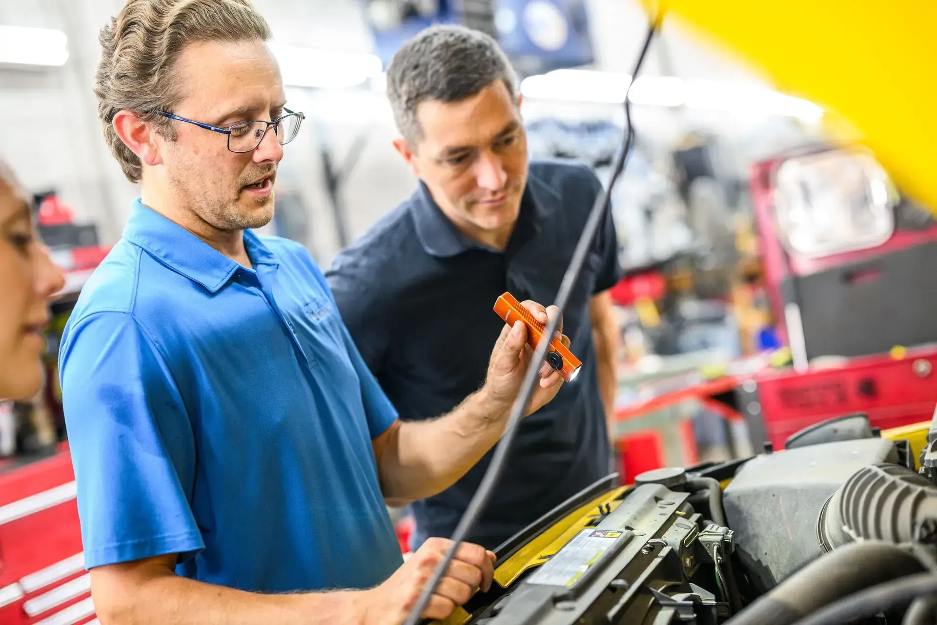 Two men examining a car engine in a garage; one holds a flashlight | Autopia Auto Repair - Bloomington
