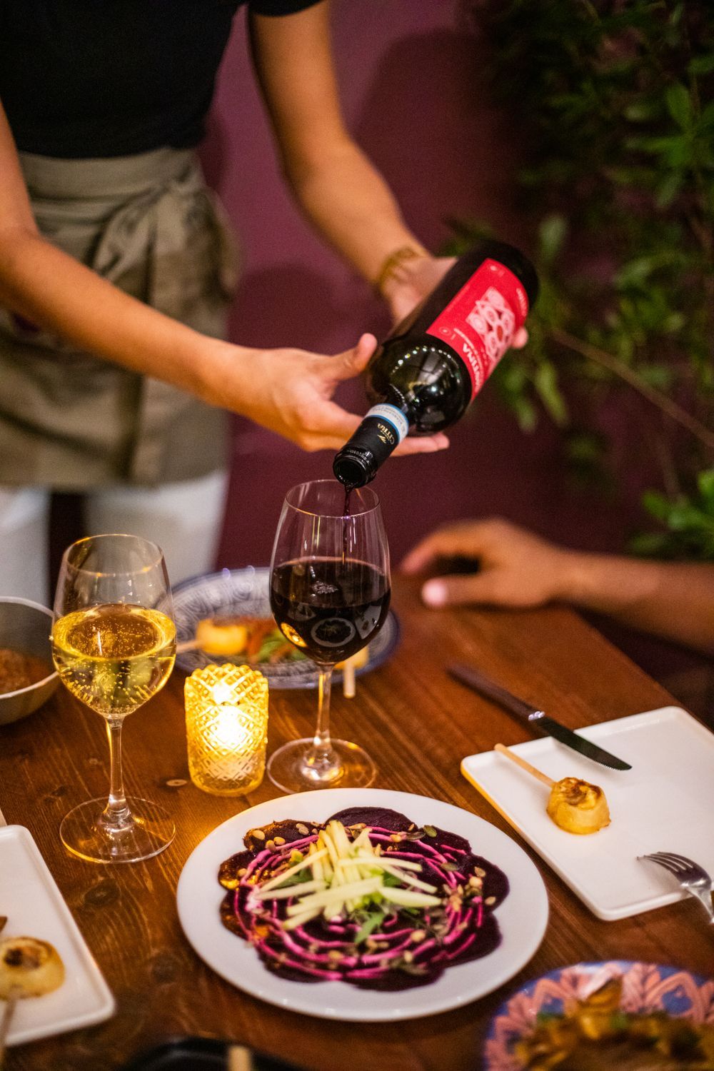 A woman is pouring wine into a glass on a table.