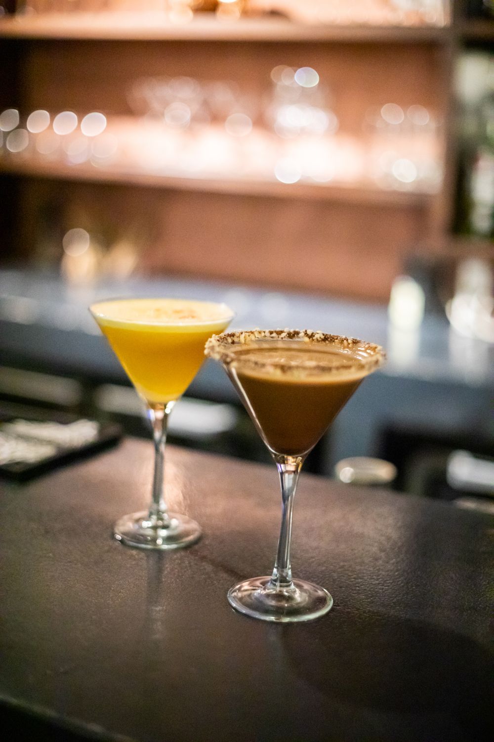 Two martini glasses are sitting on a bar counter.