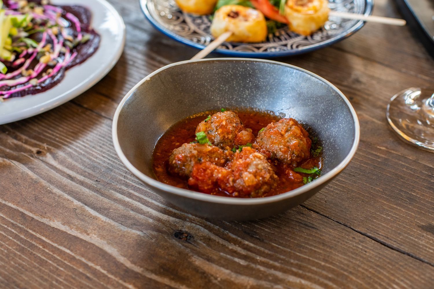 A bowl of meatballs in tomato sauce on a wooden table.
