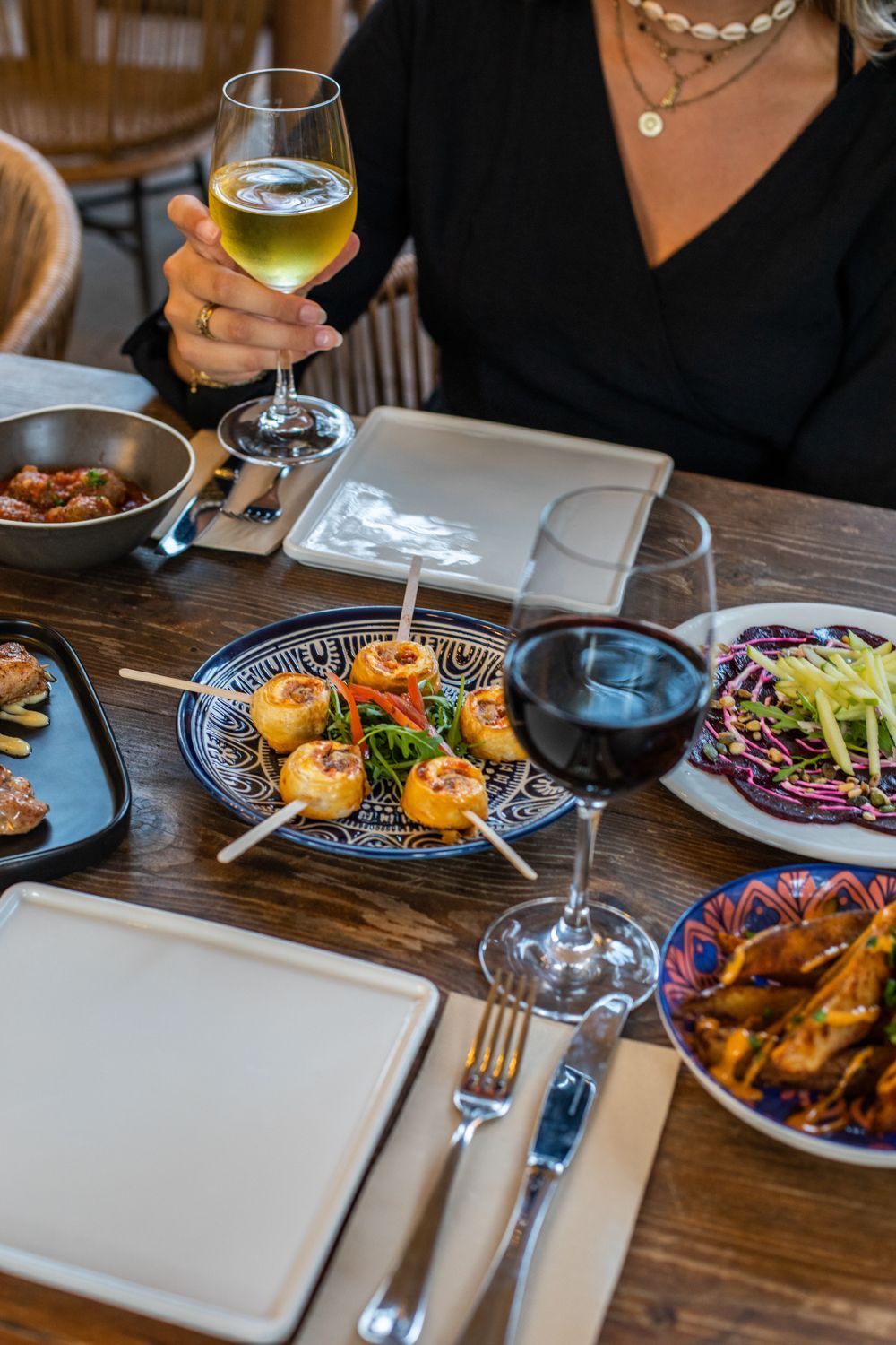 A woman is sitting at a table with plates of food and a glass of wine.