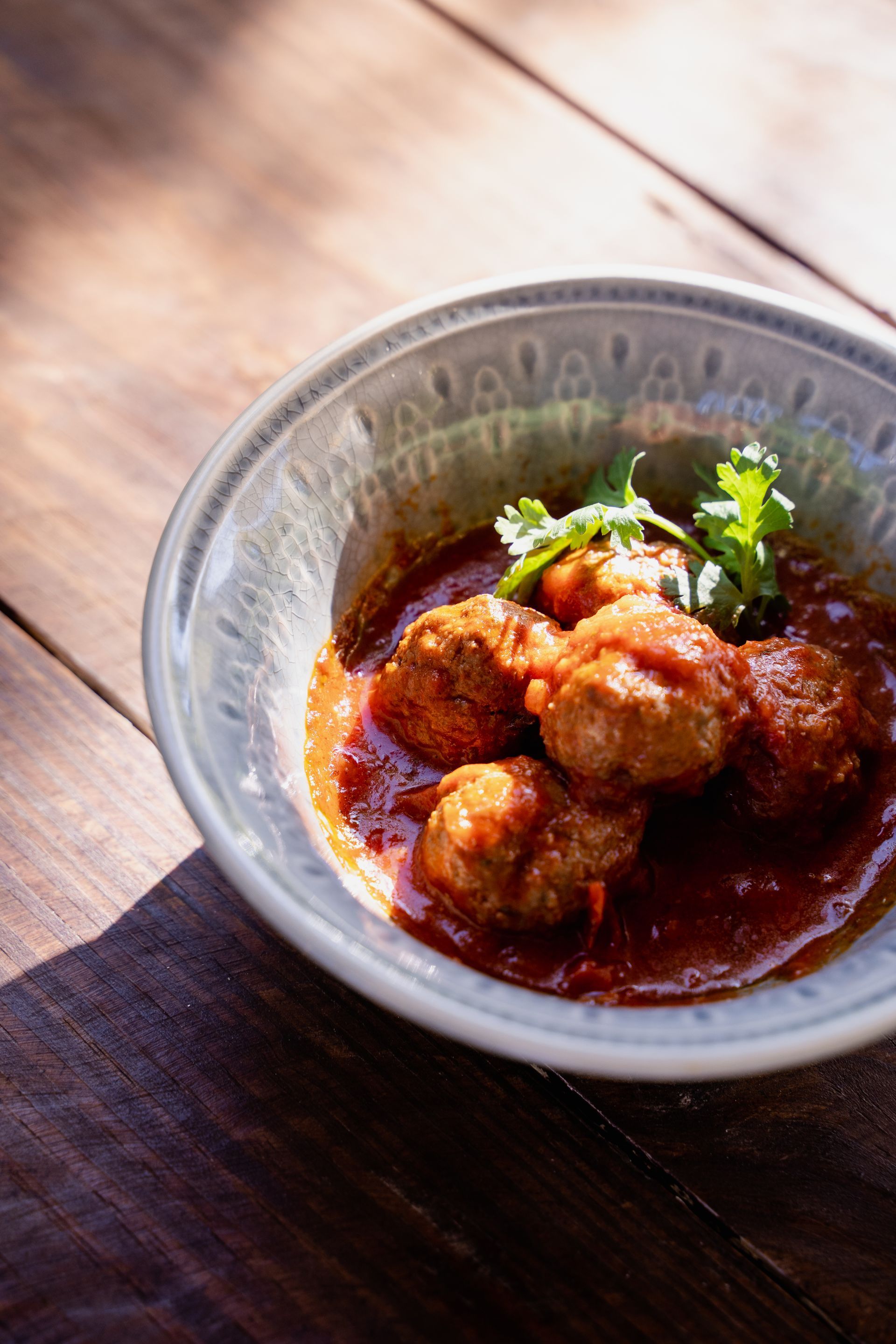 A bowl of meatballs in tomato sauce on a wooden table.