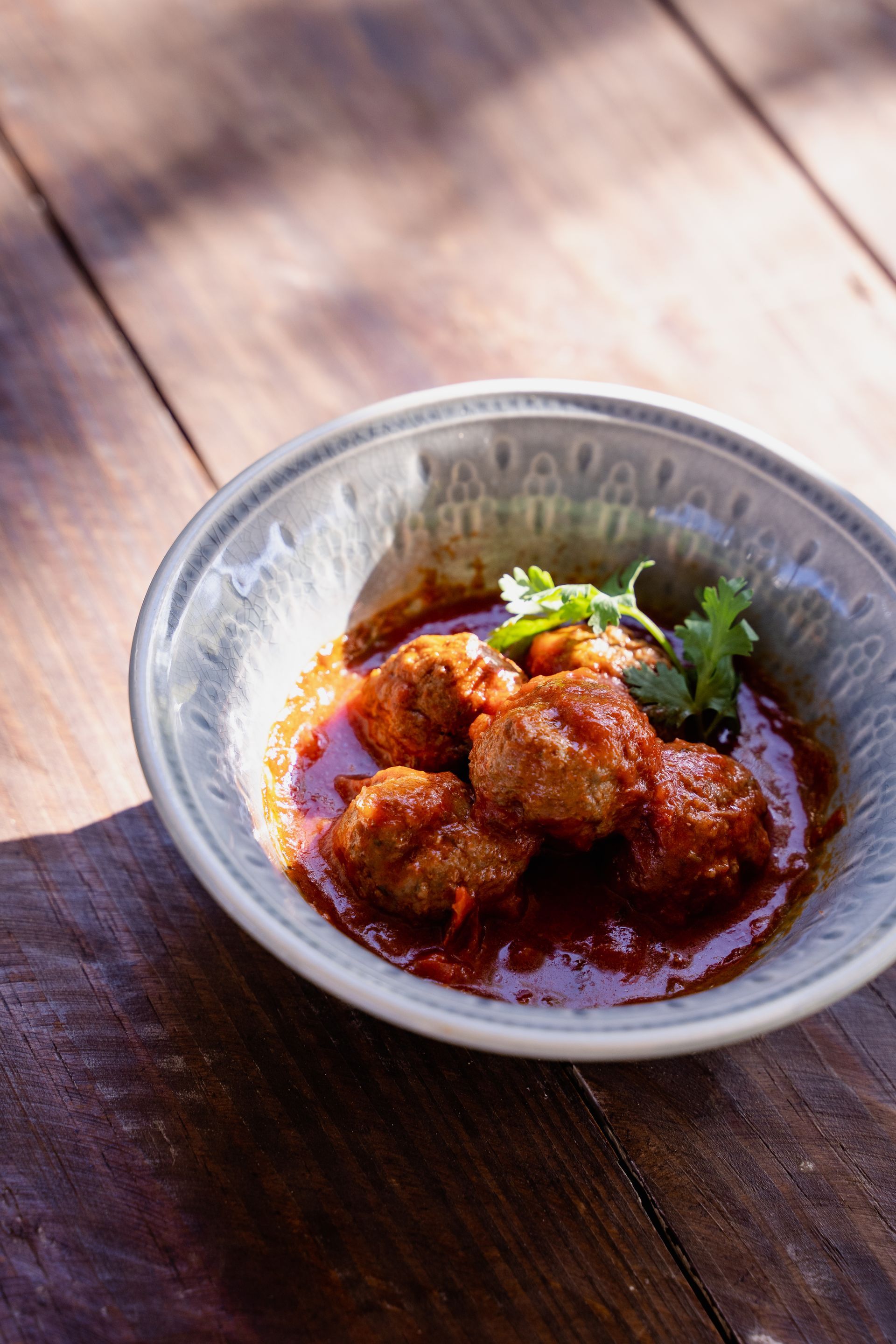 A bowl of meatballs in a sauce on a wooden table.