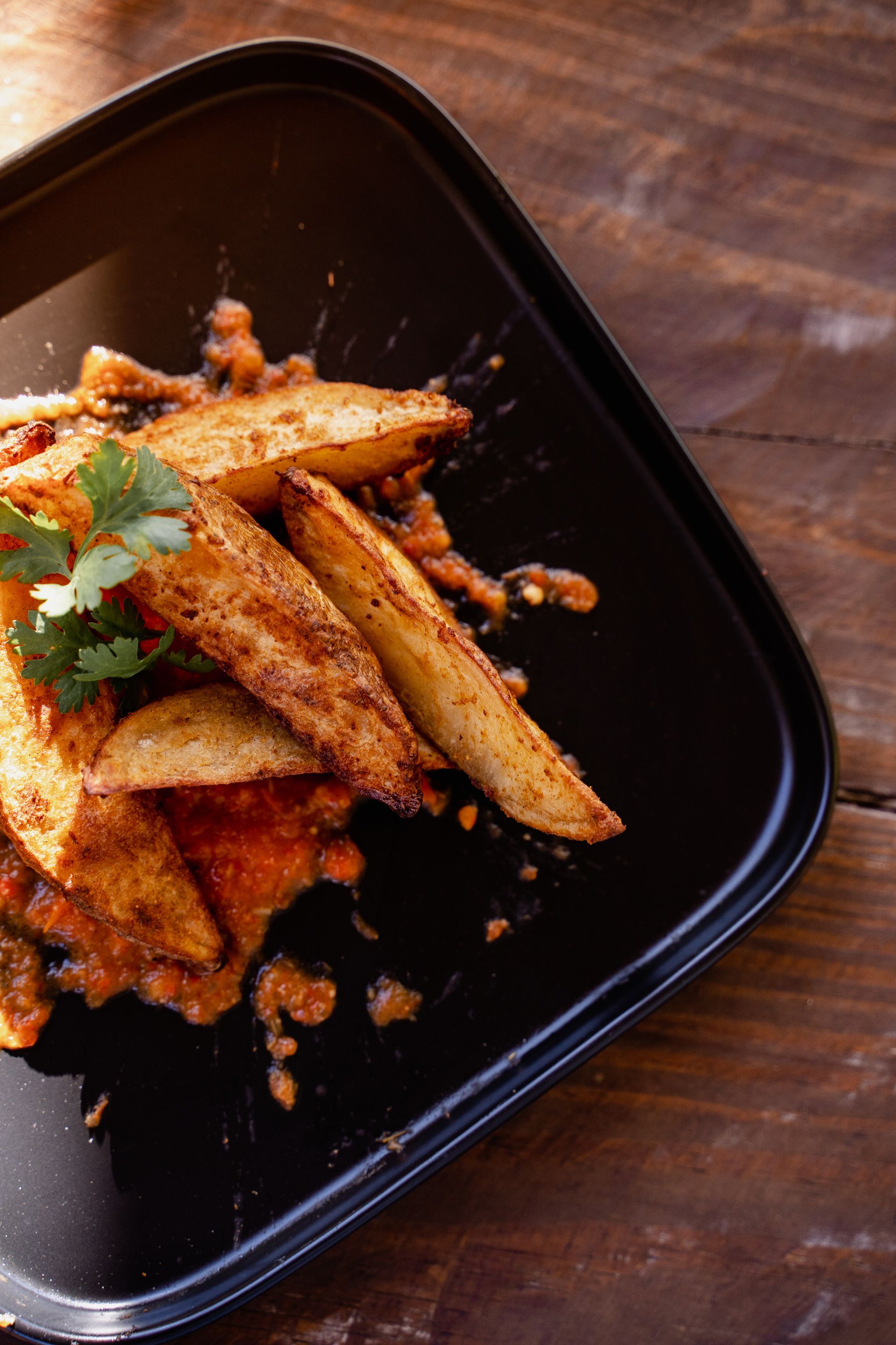 A black plate topped with french fries on a wooden table.
