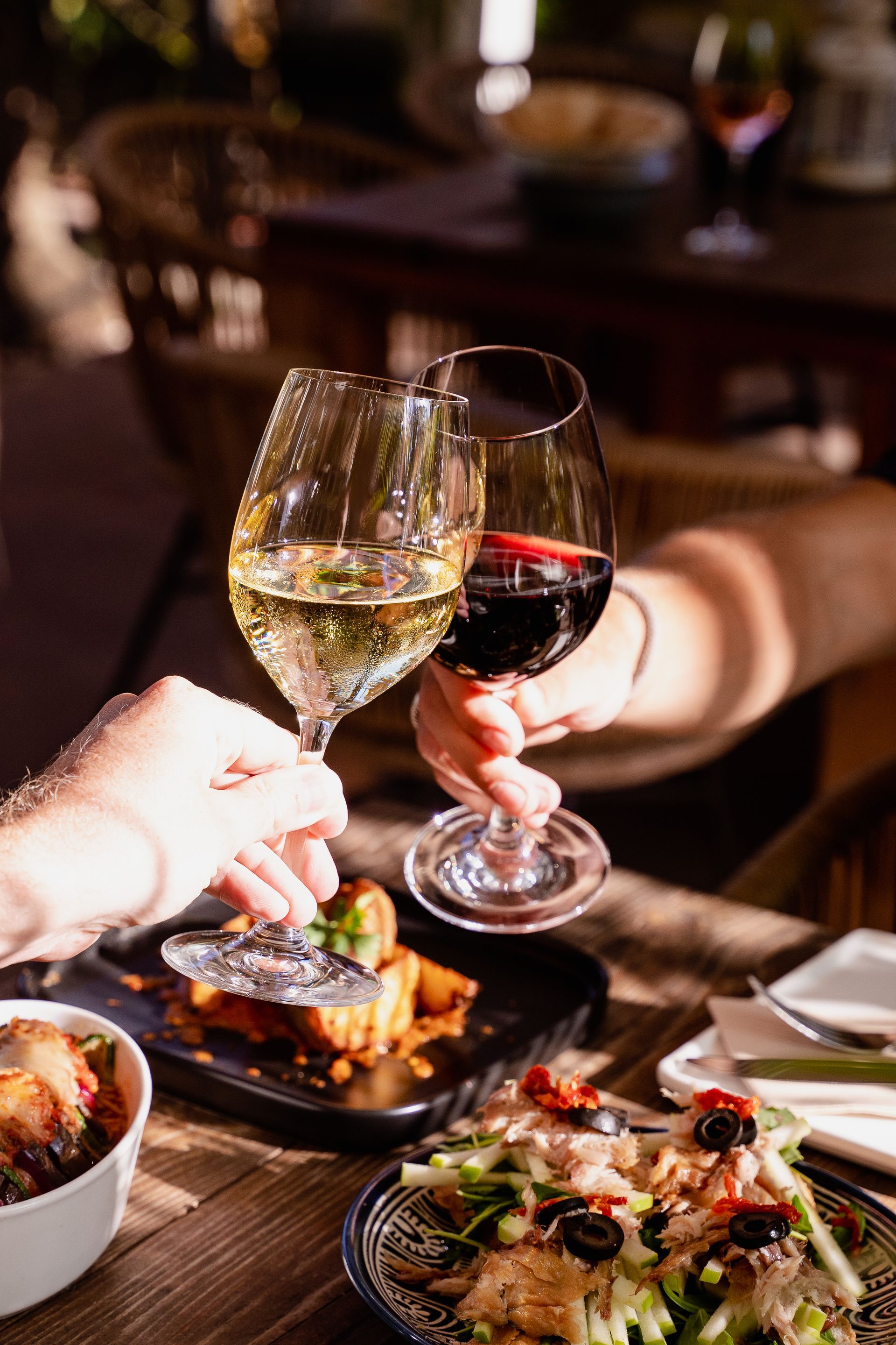 Two people are toasting with wine glasses at a table with food.
