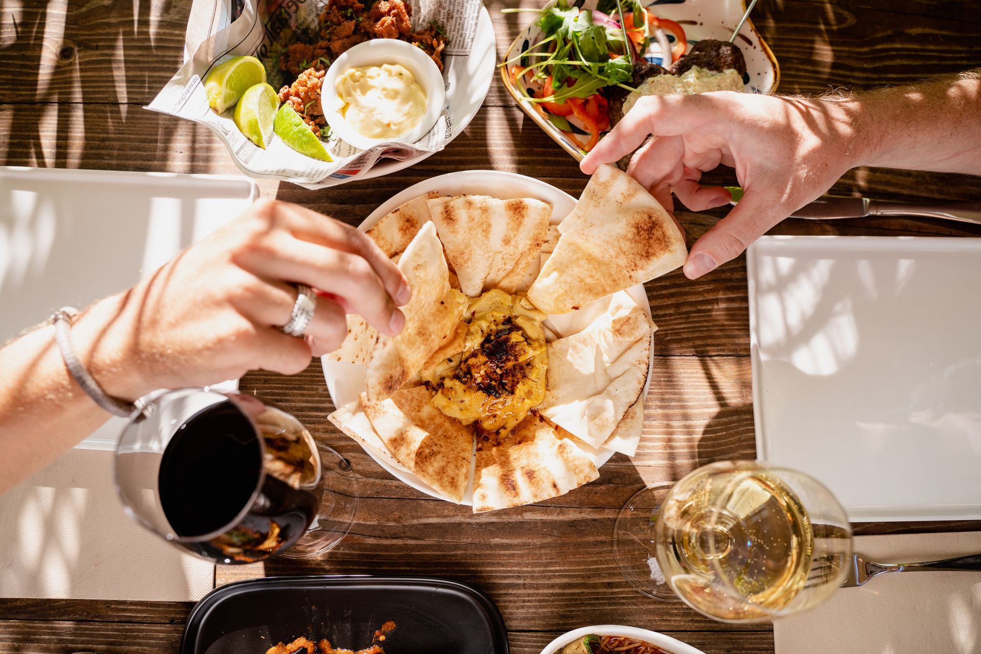 A couple of people are sitting at a table eating food and drinking wine.