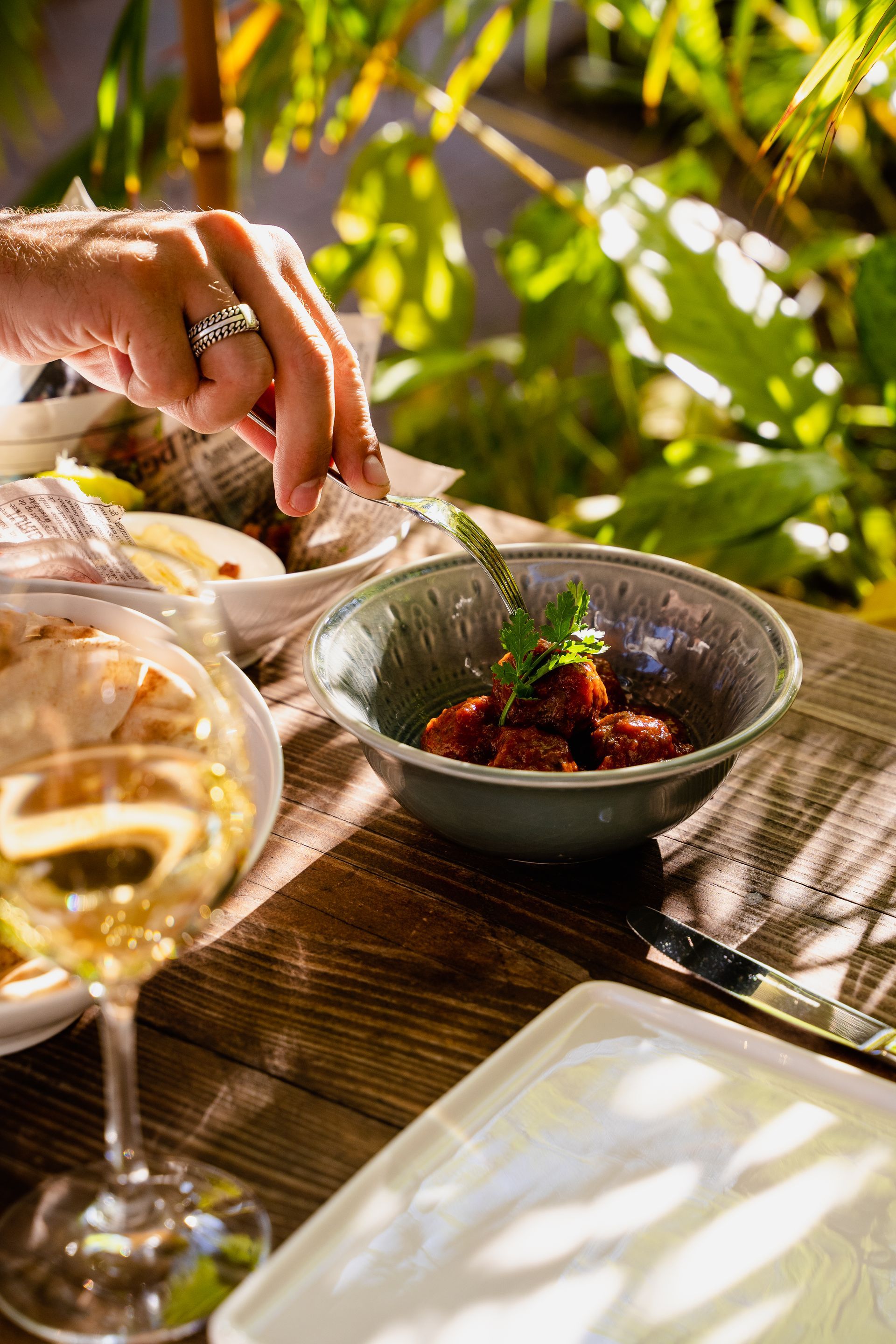 A person is sitting at a table with a bowl of food and a glass of wine.