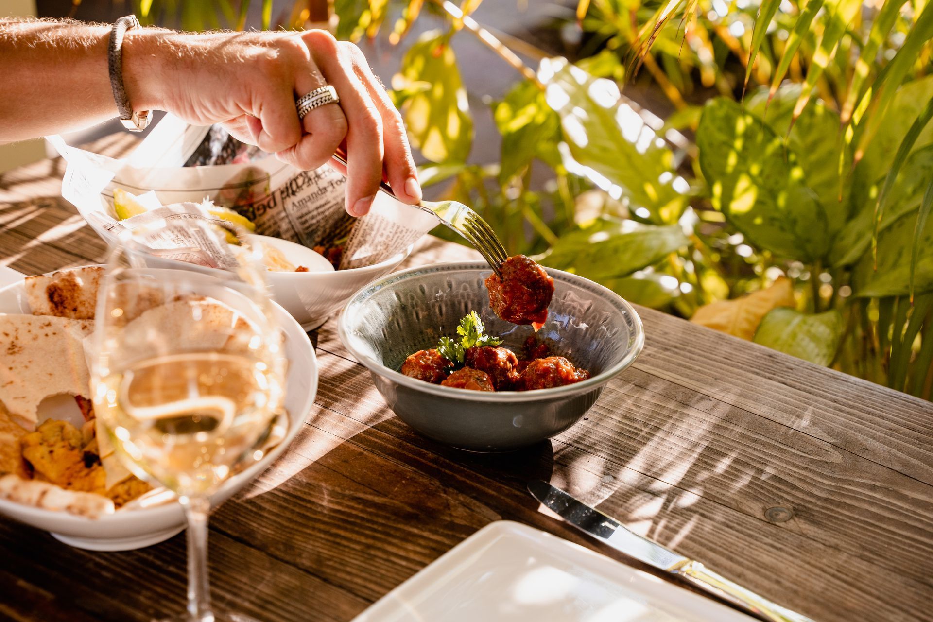 A person is sitting at a table with a bowl of food and a glass of wine.