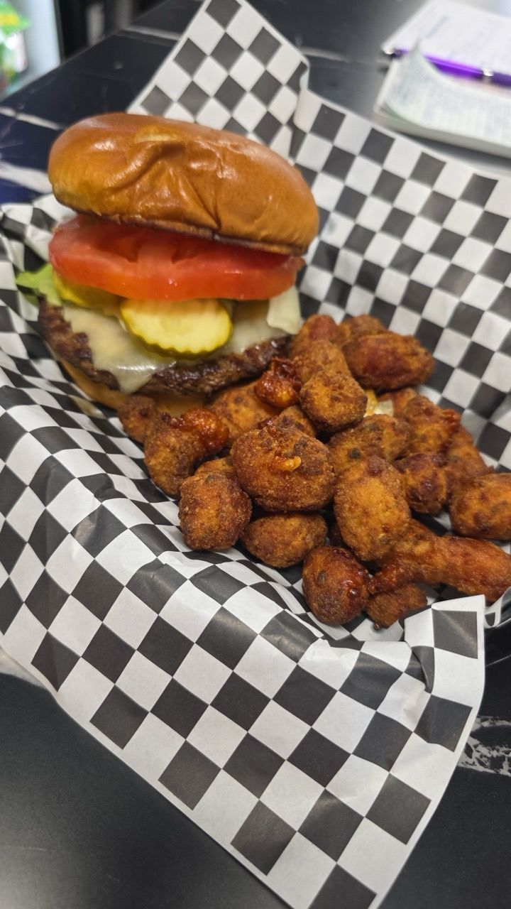 Burger and fries on a wooden board with a drink in a metal basket, against a blurred restaurant background